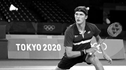Männlicher Athlet mit Schläger in Aktion in einer Halle vor einem "TOKYO 2020"-Banner